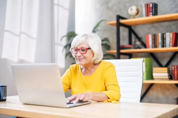 Femme âgée utilise un ordinateur portable pour travailler à l'intérieur — Photo