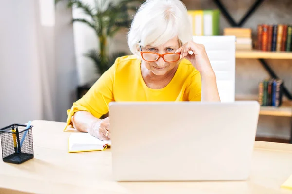 Femme âgée utilise un ordinateur portable pour travailler à l'intérieur — Photo