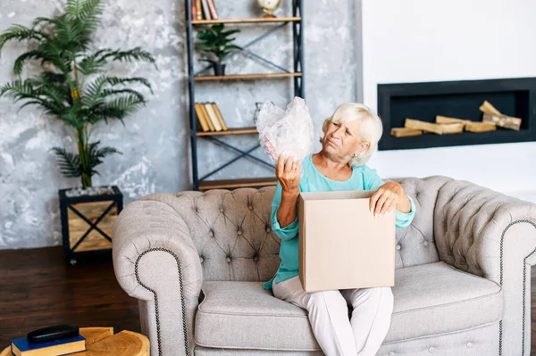 Senior woman is unpacking a cardboard box — Stock Photo, Image