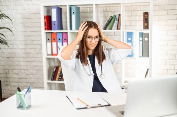 Upset young female doctor looking at laptop