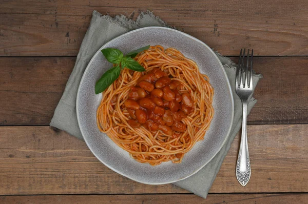 Vegetarian pasta stewed beans in tomato sauce on wood background.