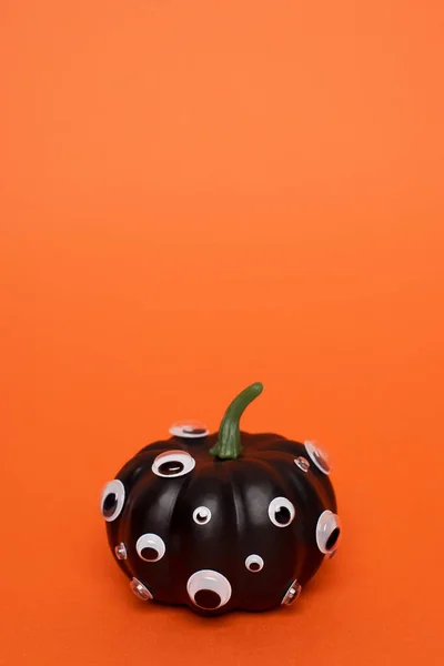 Black pumpkin with many eyes on orange background.