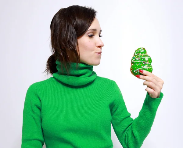 beautiful girl in a green sweater bit her lip and looks with a desire to eat a Christmas donut in the form of a Christmas tree