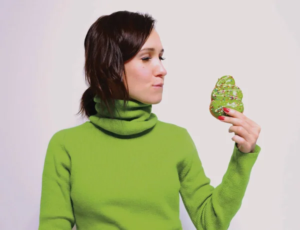 beautiful girl in a green sweater bit her lip and looks with a desire to eat a Christmas donut in the form of a Christmas tree