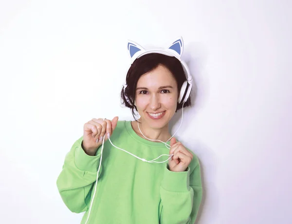 young girl in a green sweatshirt, and headphones, she listening to music and smile. headphones in the form of cat ears.