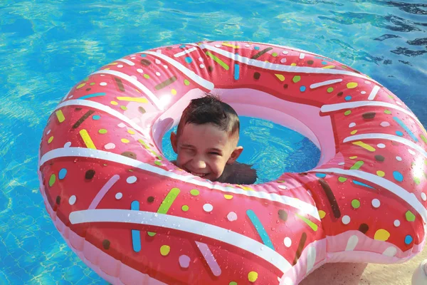 幸せなかわいい男の子でザ プールで晴れた日に上の空気マットレスでピンクのドーナツの形 — ストック写真