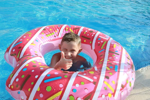 幸せなかわいい男の子でザ プールで晴れた日に上の空気マットレスでピンクのドーナツショーのような形で — ストック写真