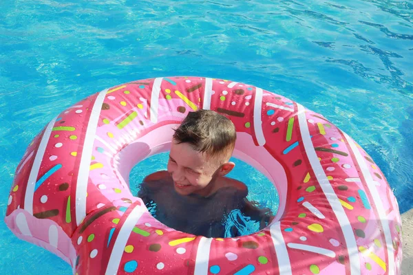 幸せなかわいい男の子でザ プールで晴れた日に上の空気マットレスでピンクのドーナツの形 — ストック写真