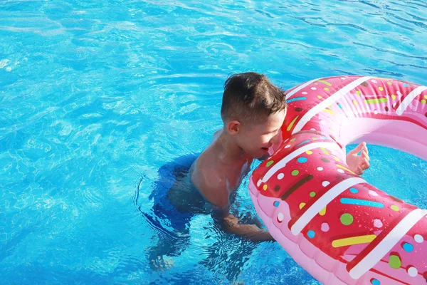 阳光明媚的日子 快乐可爱的男孩在游泳池里的空气床垫上 粉红的甜甜圈 — 图库照片