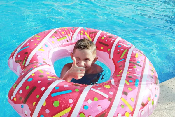 一个阳光灿烂的日子 快乐可爱的男孩在游泳池里的空气床垫上 粉红的甜甜圈表演 — 图库照片