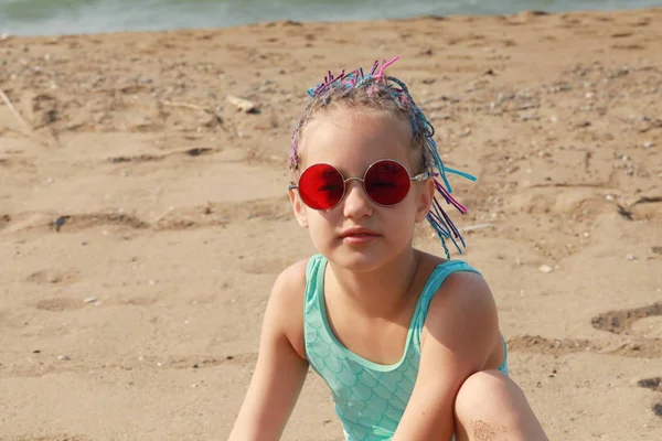 Nettes Mädchen Modischer Roter Brille Und Farbigen Zöpfen Sitzt Strand — Stockfoto