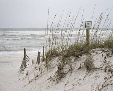 Fırtınalı bir günde ıssız sahilde kum tepeleri kapalı tutmak için uyarı teşkil imzalamak.
