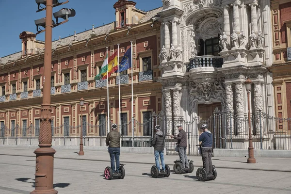 Abril 2019 - la gente en scooter patín eléctrico inteligente hoverboard manera alternativa si visita la ciudad y la vista del Palacio de San Telmo, Sevilla, España. Sede de la presidencia en un día soleado . — Foto de Stock
