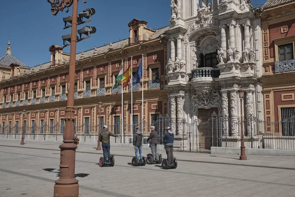 Abril 2019 - la gente en scooter patín eléctrico inteligente hoverboard manera alternativa si visita la ciudad y la vista del Palacio de San Telmo, Sevilla, España. Sede de la presidencia en un día soleado . — Foto de Stock