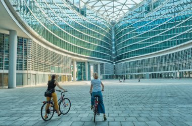 Milano İtalya - Temmuz 2019 modern bir bina cam bisiklet soyut yapılar ile şehir keşfetmek iki kadın.