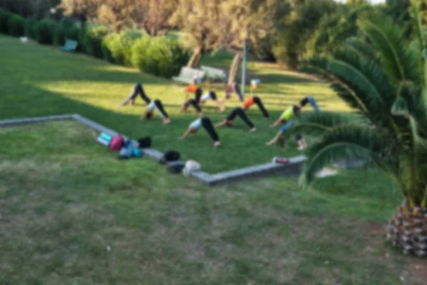 Personas que practican yoga en el parque al atardecer - fuera de foco y fondo borroso . — Foto de Stock