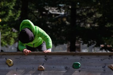 Güneşli bir günde çocukların oyun parkında tırmanma duvarında oynayan bir çocuk.