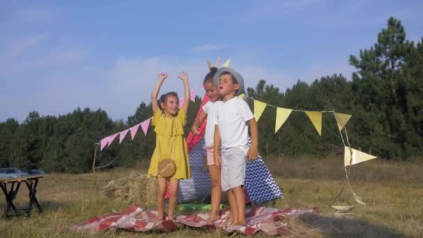 Barnens glädje, glada barn vänner har kul hoppning och sång mot bakgrund av Wigwam under sommarlovet i ängen i skogen — Stockvideo