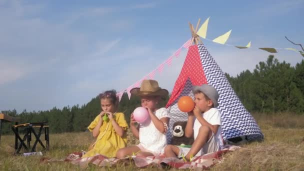 子供のピクニックゲーム、面白い男の子と女の子は、新鮮な空気で週末にウィグワムを飾るためにカラフルなボールを膨らませるために幸せです、 — ストック動画