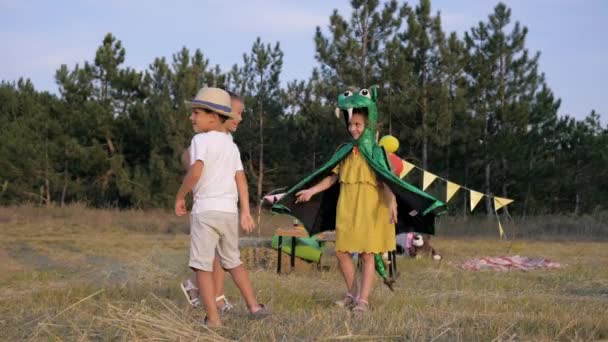 Permainan anak-anak, perempuan kecil berkostum naga berjalan dengan teman-temannya yang ceria dalam pembersihan selama piknik di latar belakang hutan wigwam — Stok Video