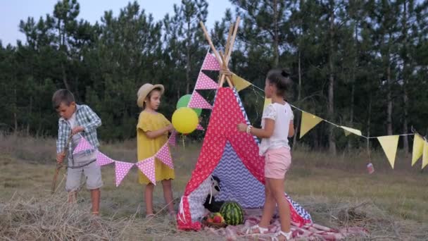 Amigos decorar uma clareira com wigwam em uma floresta para um piquenique durante um fim de semana no campo, infância feliz — Vídeo de Stock