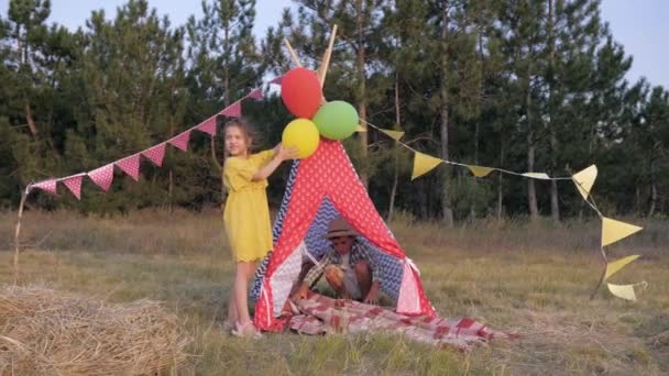 Malé zdobí mýty balóny a piknikovým přikrývkou vigvamu na piknik na zábavním víkendu venku v lese během letního víkendu. — Stock video