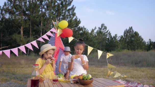Picknick eten, mannelijke kind brengt watermeloen van Wigwam naar kleine meisjes op de middageten tijdens het weekend buiten de stad op de zomerdag — Stockvideo