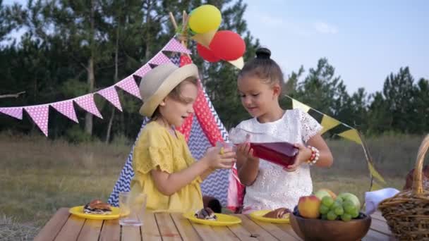 Picnic en el bosque, pequeñas hembras felices niños sacian su sed, beber jugo en el almuerzo durante el viaje al campo en el fondo de wigwam — Vídeos de Stock