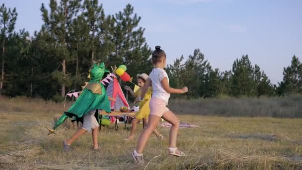 Wochenendspiele im Wald, aktive Kinder auf einer Lichtung, die mit Pergwam dekoriert ist, fangen einander im Drachenkostüm beim Picknick — Stockvideo