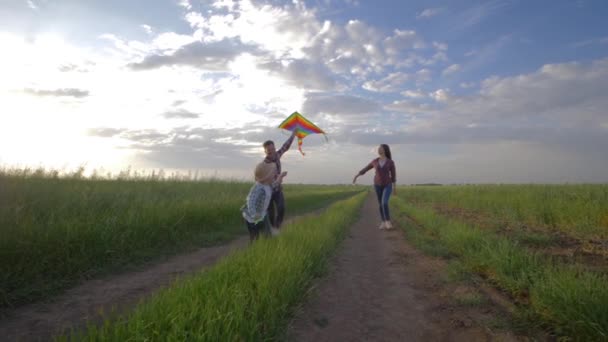 Enfance joyeuse, enfant avec cerf-volant dans les mains court près de jeunes parents à la campagne pendant les loisirs de plein air — Video