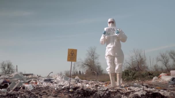 Junge Frau in Uniform und Schutzbrille mit Plakat auf Müllhalde in Gummistiefeln nahe Schild für biologische Gefahr — Stockvideo