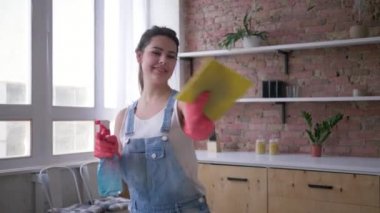 denim tulum ve eldiven mutlu ev hanımı mutfak temizliği sırasında elinde temizleyici sprey ve duster ile dans
