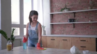 bahar genel temizlik, eldiven kadın bez ve temizleyici sprey ile masa temizleme sonra kamera ve mutfakta gülümsüyor görünüyor