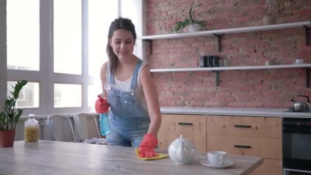 Házimakkal és a háztartás, a gyönyörű nő kesztyűt tisztító spray és a poroló törli asztalra, majd úgy néz ki a kamera a konyhában — Stock videók