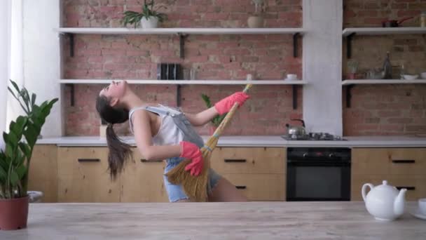 Кухонная уборка, счастливая домохозяйка в джинсовом комбинезоне и перчатках танцует и играет на метле, как гитара — стоковое видео