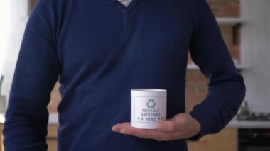 kullanılan pilleri toplama, adam uluslararası geri dönüşüm logosu üç kovalayan oklar ile konteyner içine eski piller koyar sonra başparmak kadar jest göstermek