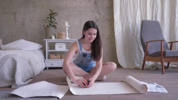Reparatie en huisverbetering, meisje met potlood en meetlint maakt merken op nieuwe behang roll op de vloer — Stockvideo