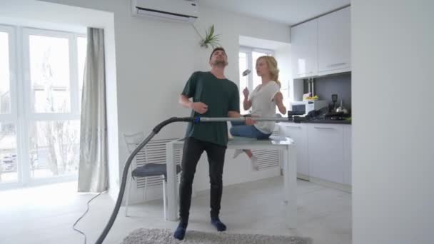 Couple amoureux s'amuse dans la cuisine, homme heureux danse avec aspirateur avec fille qui chante avec une louche comme un microphone — Video