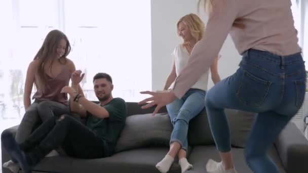 Друзья бегают и прыгают на диване и танцуют под гитару, мальчики и девочки веселятся на домашней вечеринке — стоковое видео