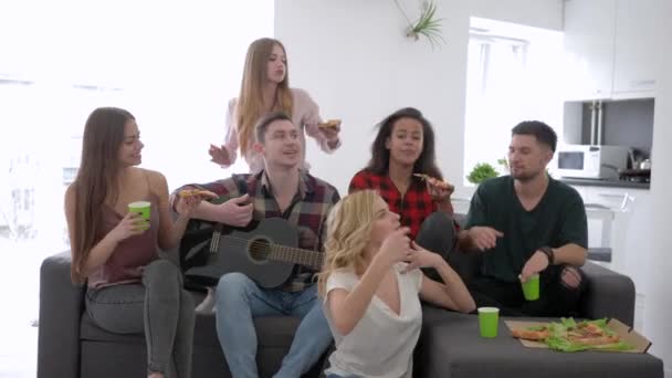 Amigos cantando con guitarra y comiendo pizza sentados en el sofá en casa fiesta, amistad y relación — Vídeo de stock