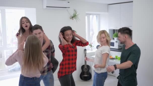 Amigos jugando con confeti en la cocina en cámara lenta, los jóvenes multirraciales están bailando y divirtiéndose en una fiesta en casa — Vídeo de stock
