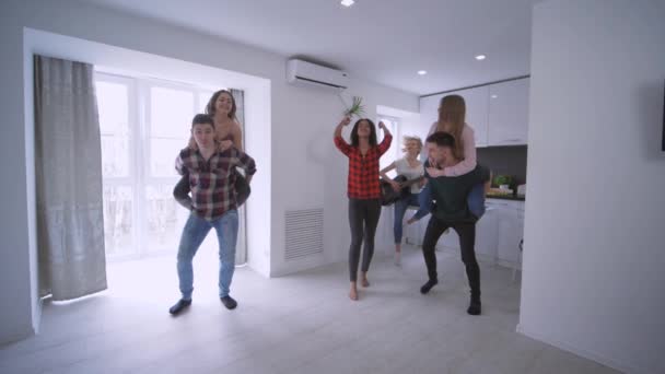 Multinational friends having piggyback races against each other in apartment enjoying holidays at home party in slow motion — Stock Video