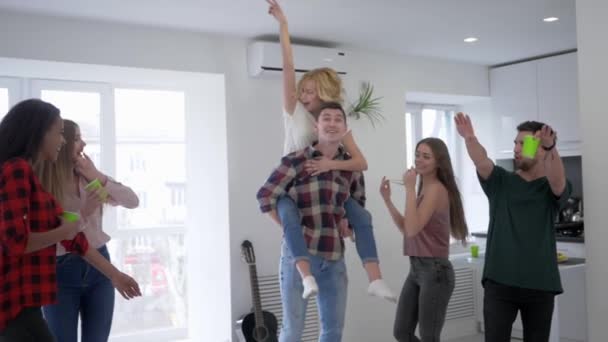 Jongeren zijn gek rond op een Home Party, jongens en meisjes dansen en plezier hebben in de keuken met plastic glazen in hun handen — Stockvideo