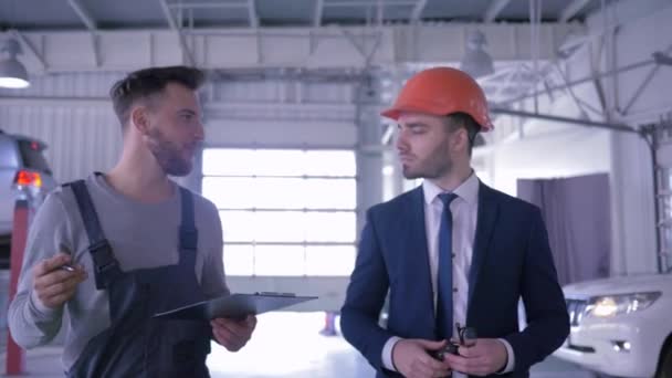 Auto mechanic advices customer in hard hat and shows the state of machines at repair station — Stock Video