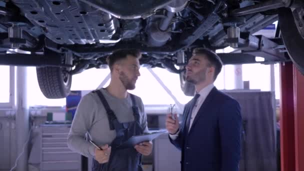 Oto mekanik denetimler teknik durum araç araba hizmeti müşteri ile mekanik asansör sonra mutlu erkekler el sıkışmak ve kamera bakmak — Stok video