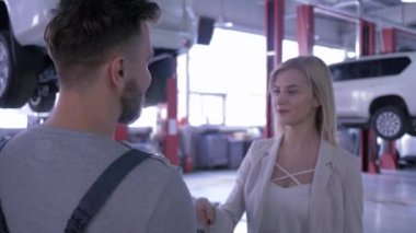 kadın müşteri oto tamir servisi temsilcisi ile el sıkışıyor ve hidrolik asansör aracın arka planda araç anahtarları verir