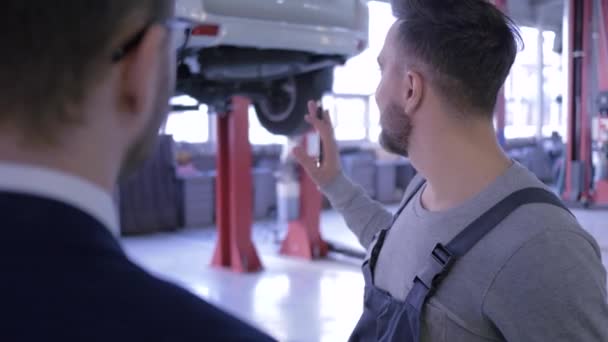 Mecánico con portapapeles explicando los gastos de reparación de automóviles a su cliente y estrechando las manos en el taller — Vídeos de Stock