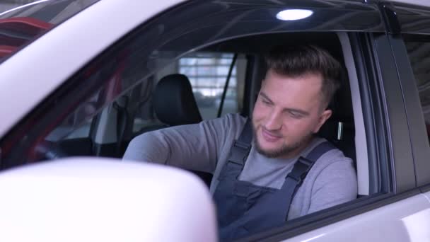 Retrato de hombre mecánico feliz sentado detrás del volante de un coche nuevo con una sonrisa mira a la cámara con las llaves en la mano — Vídeo de stock