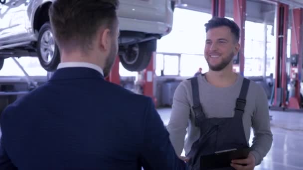 Mecanician masculino profissional e proprietário do carro falando e apertando as mãos no fundo do automóvel em um elevador, bom negócio — Vídeo de Stock