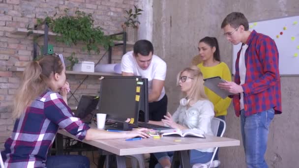 Discusión de negocios, compañeros de trabajo jóvenes hablan con asociado de oficina que trabaja en la computadora — Vídeo de stock